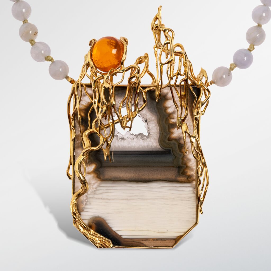 Jean VENDOME_Collier présentant un pendentif en or jaune 18k (750 millièmes) serti d'une tranche d'agate surmontée d'une opale de feu, la monture stylisée de branchages tortueux, le tour de cou formé de billes de calcédoine. Poinçon de maître. Pièce unique. Poids brut : 59,4 g. Dim. du pendentif : 7,3 x 4,5 cm Tour de cou : 47 cm