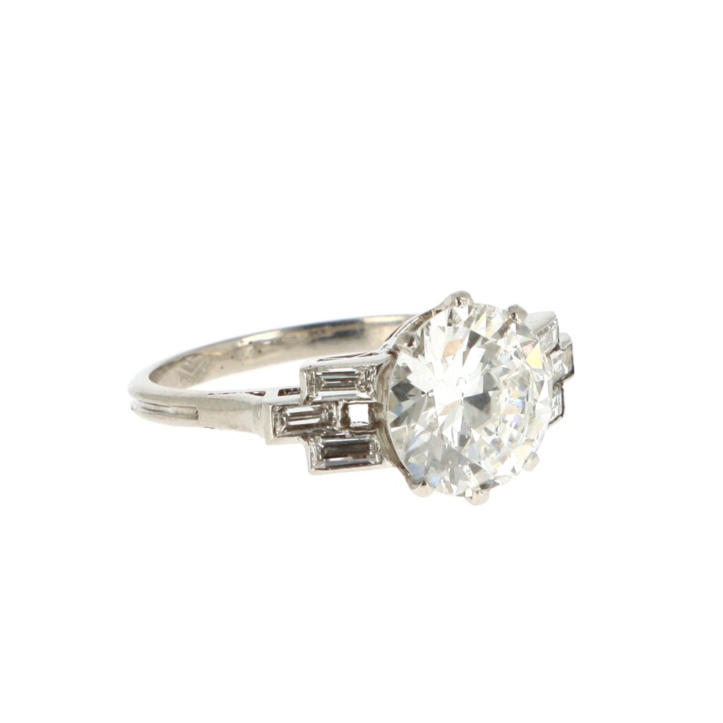 Adjugé 10 000 €_Bague diamant solitaire_Bague en platine (950 millièmes) sertie d'un diamant rond taille brillant de 2,45 carats, épaulé de six diamants baguettes.Travail français vers 1930. Dim. diamant : 9.05 - 9.10 x 4.91 mm Poids brut : 4,2 g