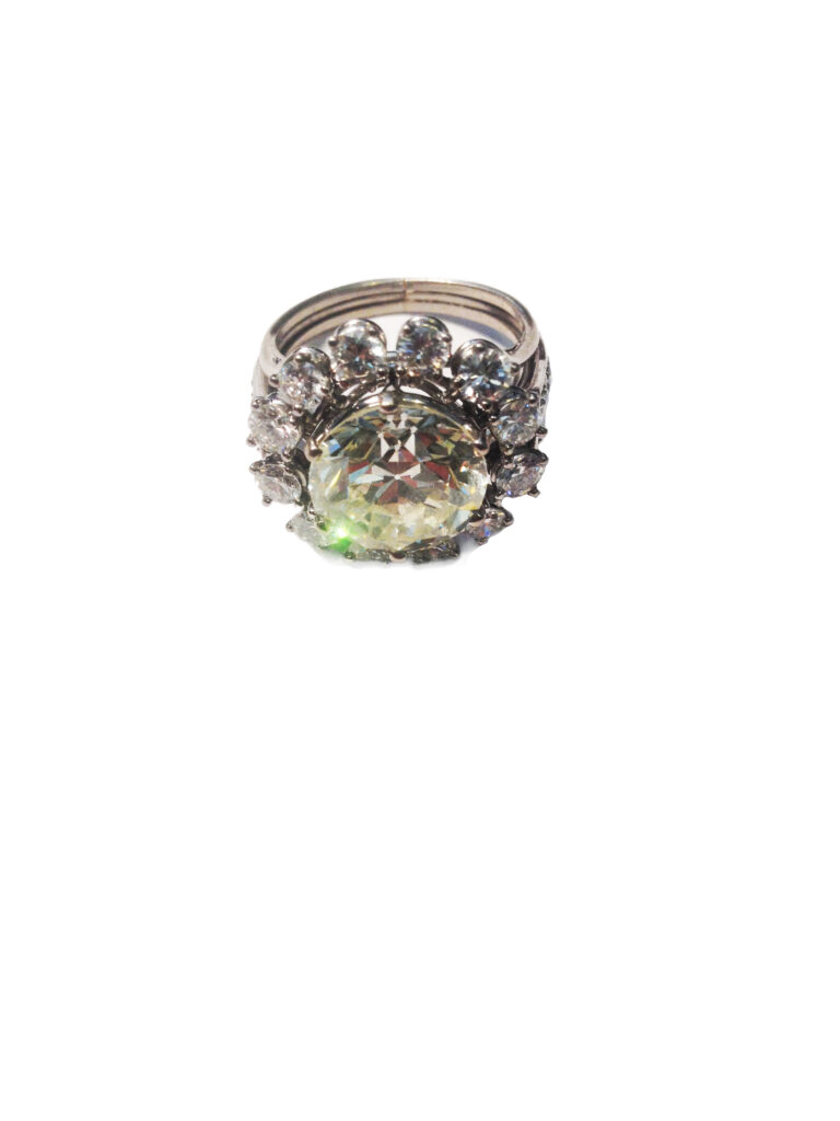 C1403-0871_Adjugé 21 000_Bague en or gris 18 k. Elle stylise une fleur. Le pistil est orné d'un diamant demi-taille d'environ 5 cts. Il est disposé dans un entourage de douze brillants. Le corps de bague est également agrémenté de quatre brillants. Tour de doigt: 53. Poids brut: 8,3 g.