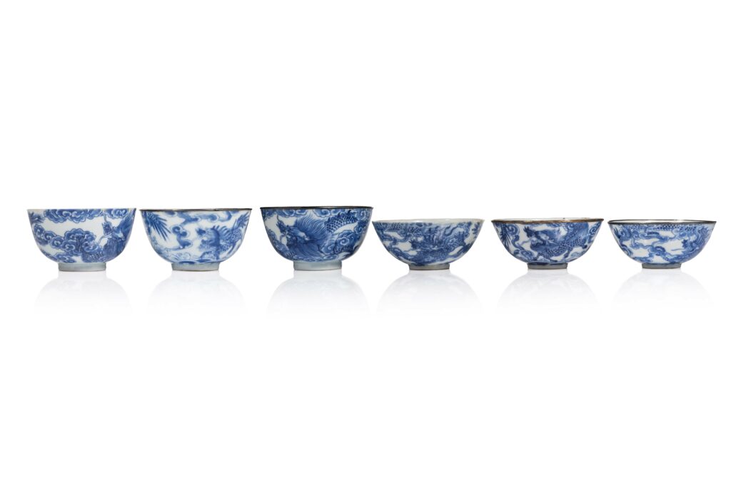 N0578-0009 VIETNAM, XIXe siècle,Ensemble de six coupes en porcelaine "Bleu de Hué" Montés sur des petits pieds, à parois arrondies, présentant des décor en bleu de cobalt sur fond blanc de dragons, phénix et ky lan pourchassant la perle sacrée parmi les nuées. Marques « Nhât » (日) sous les bases. Quatre comportant des cerclages métalliques en bordure. Hauteur : 4 et 5.5 cm Diamètre : 9.8 et 10 cm Adjugé 14 000 €