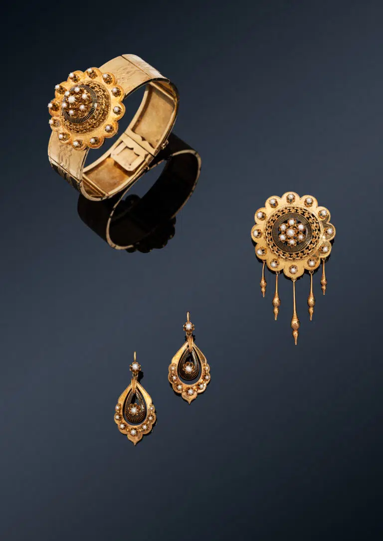 Parure or et perles - Parure en or jaune 18k (750 millièmes) comprenant un bracelet, une broche et une paire de pendants d'oreilles, l'ensemble à décor ciselé souligné de demi perles* et d'émail noir. Le motif central du bracelet amovible.