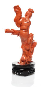 CHINE, XXe siècle, Branche de corail orange* sculptée, Description : Prenant la forme d'une élégante debout, une main relevée et l'autre tenant une branche de lotus en fleur. Fixée sur son socle en bois adapté. Hauteur : 18 cm Poids brut : 381 g