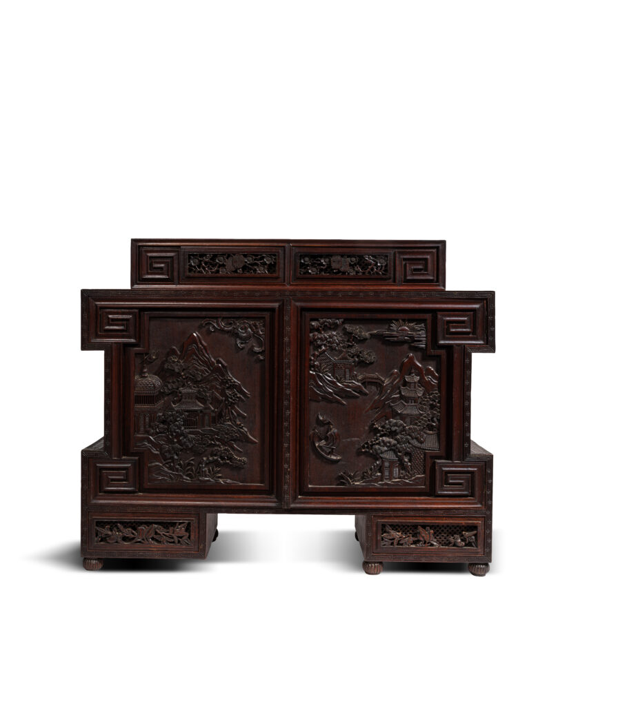 Elégant cabinet en bois sculpté, Adoptant une forme complexe, les différents encadrements et éléments le composant conférant un style géométrique à l'ensemble. Ouvrant par deux petits vantaux en façade et quatre tiroirs rectangulaire, les bordures un décor de frises de grecques imbriquées formant des réserves en saillie et accentuant la structure géométrique du meuble. Les panneaux des portes sculptés en relief de paysages montagneux animés et pavillons. Les tiroirs ajourés d’une frise de rinceaux stylisés centrés de caractères shou en médaillons. 72 x 87 x 29 cm