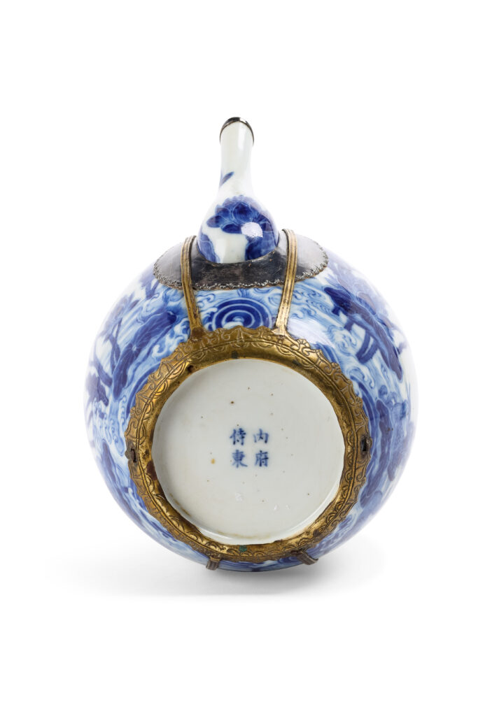 VIETNAM, fin du XVIIIe siècle - Théière en porcelaine "Bleu de Hué" - Le corps globulaire surmonté d'un col court, flanqué d'un bec verseur en "S" et accompagné d'un couvercle légèrement bombé. Présentant sur l'ensemble un fin décor en bleu de cobalt sur fond blanc d'un couple de canards évoluant parmi un étang de lotus, une frise de motifs losangiques ornant le col, le couvercle à décor d'un dragon à cinq griffes dans les nuées. Une marque "内府待東" (Nội phủ thị đông» soit « Palais intérieur enceinte de l'Est » ) à quatre caractères sous la base. Avec sa monture en laiton ciselé.