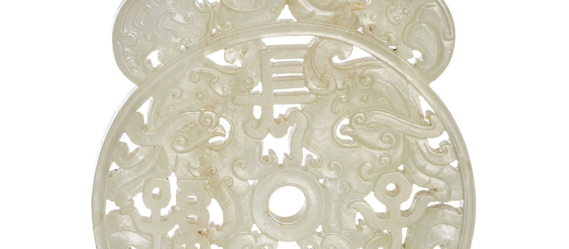 N0456-0012_CHINE, XVIIIe siècle Élément en jade céladon À décor sculpté et ajouré prenant la forme d'un disque bi comprenant quatre phénix stylisés autour d'un caractère, la partie supérieure ornée de dragons stylisés. La pierre aux tons céladon légèrement infusés de rouille. Hauteur : 12,7 cm Largeur : 7,7 cm Adjugé 28 000 €