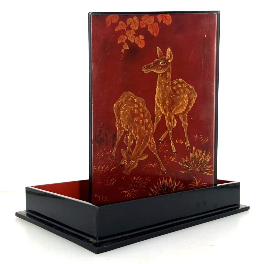 P2402-0002, de forme quadrangulaire, présentant sur le couvercle un décor en laque or et ocre sur fond rouge de deux biches dans la jungle. L’intérieur en laque rouge portant l’inscription «Tran-Phuc-Duyen, Artiste laqueur, Hanoï, Vietnam, 146 av. du Grand Bouddha». 30 x 20 cm